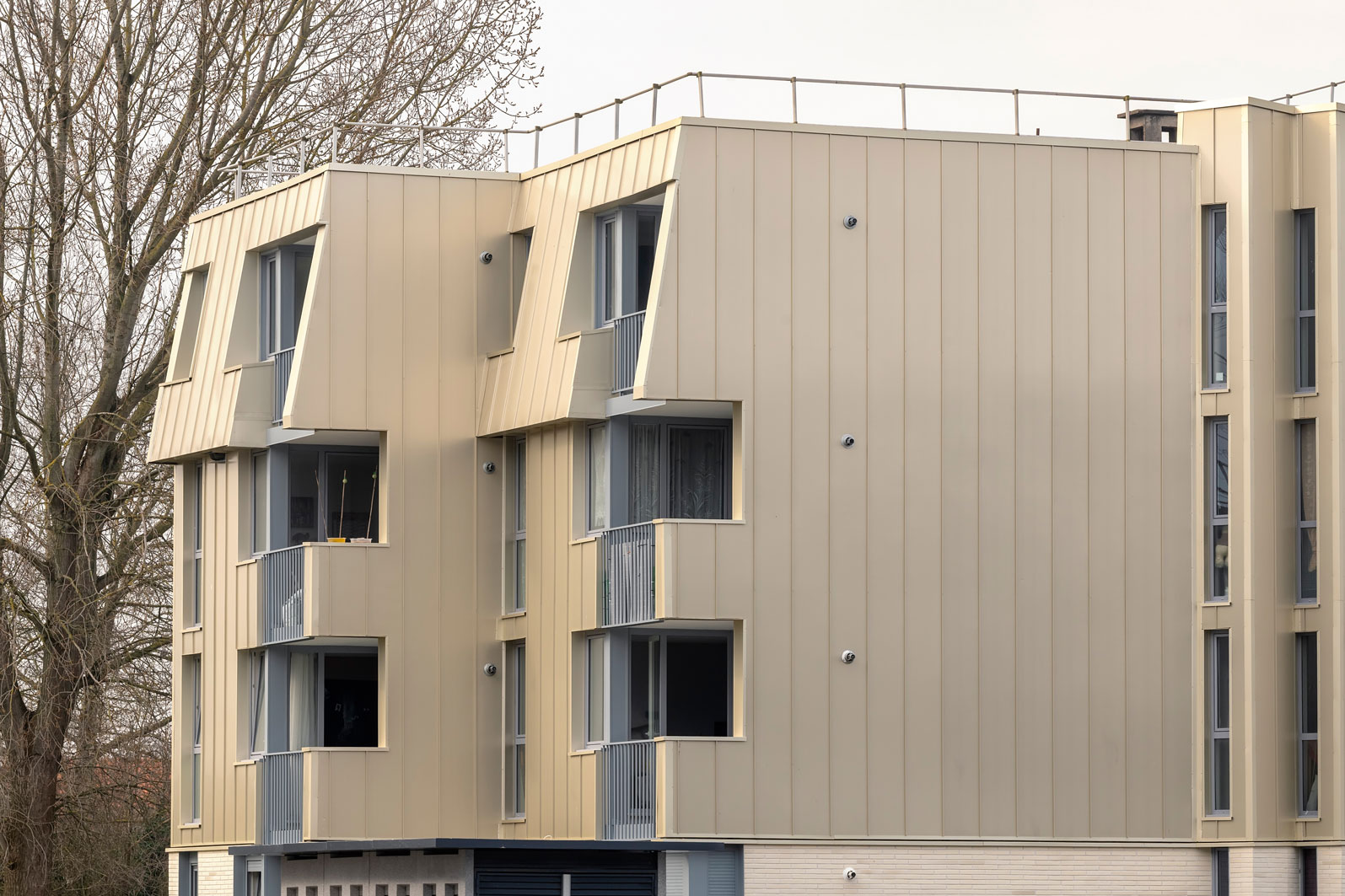 Façade de la résidence Pascal en bardage aluminium champagne, murs droits et brisis inclinés en joint debout